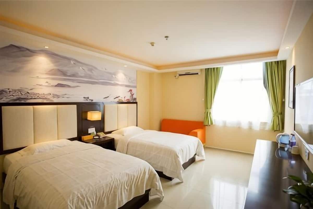 Una habitación de hotel con dos camas, un escritorio, una silla, un televisor y un mural en la pared.