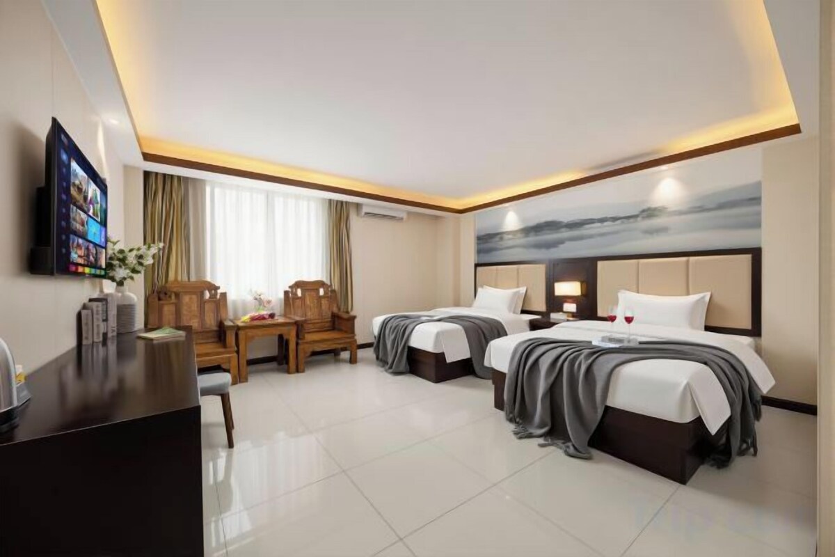 A hotel room with two beds, a desk, a TV, and a painting on the wall.