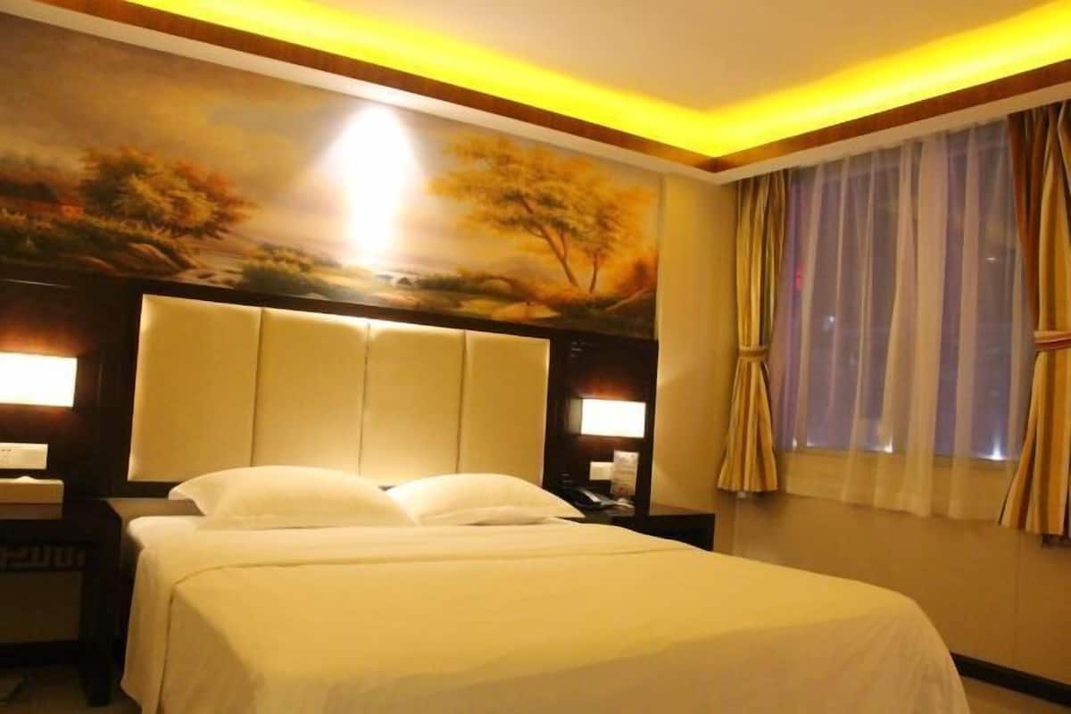 Habitación de hotel con una cama grande, cabecero con iluminación integrada, un cuadro en la pared y una ventana con cortinas.