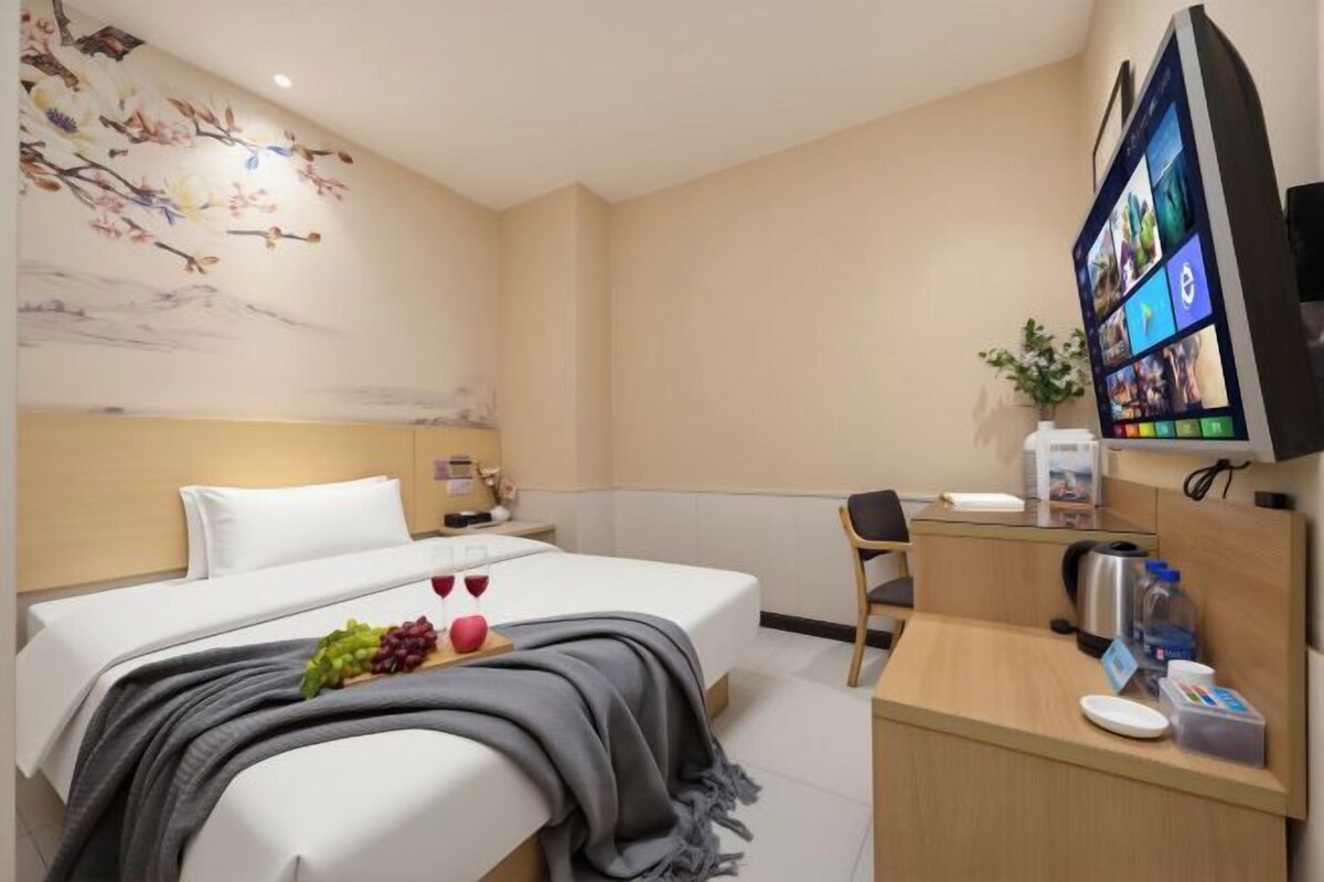 A hotel room with a bed, a desk, a television, and a wall-mounted screen.