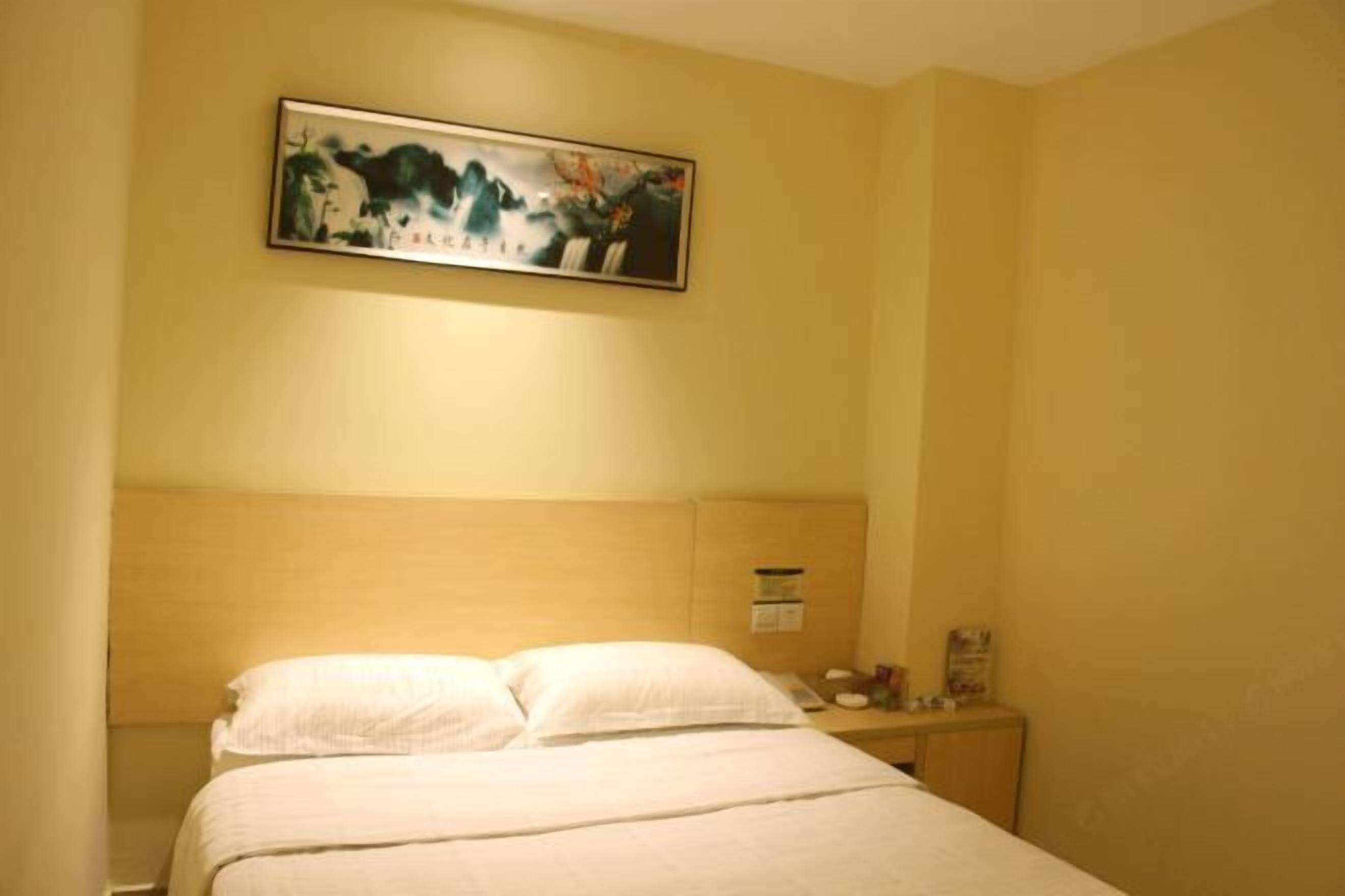A hotel room with a bed, a nightstand, and a painting on the wall.