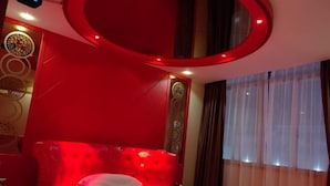 Una habitación con cabecera tapizada en rojo, cama con ropa blanca y lámpara circular en el techo.