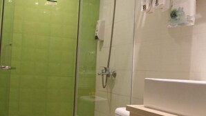Un baño con ducha de vidrio, inodoro blanco y encimera color beige con lavamanos.