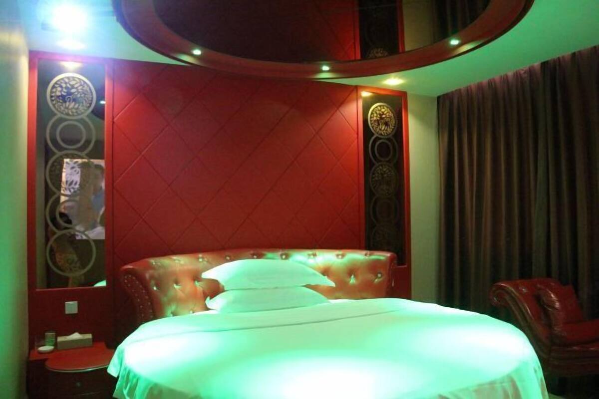 Un dormitorio con cabecera capitonada, cama con ropa de cama blanca y una pared de acento roja.