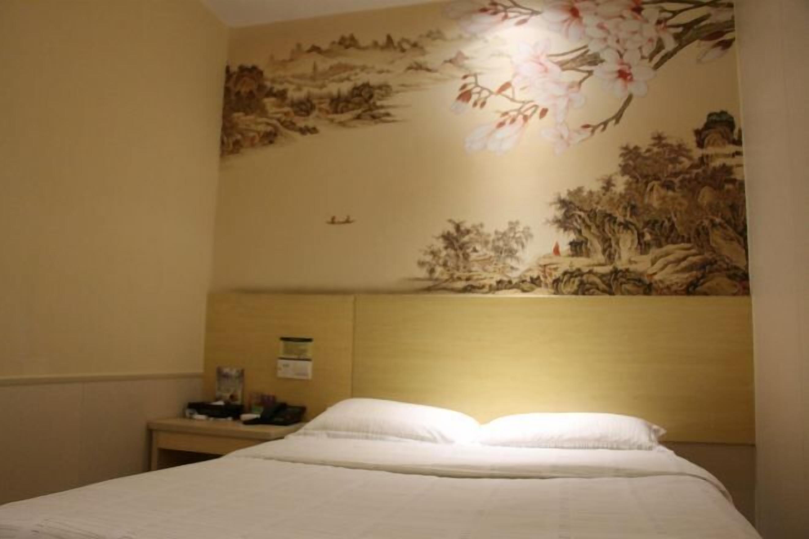 Ein Hotelzimmer mit Bett, Nachttisch und Wand mit floralem Wandgemälde.