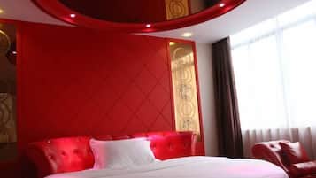 Quarto de hotel com cabeceira estofada em vermelho, espaldar branco e poltrona de couro vermelha.