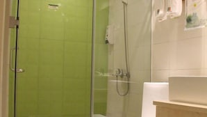 Un baño con ducha envuelta en vidrio, inodoro blanco y lavamanos con encimera color beige.