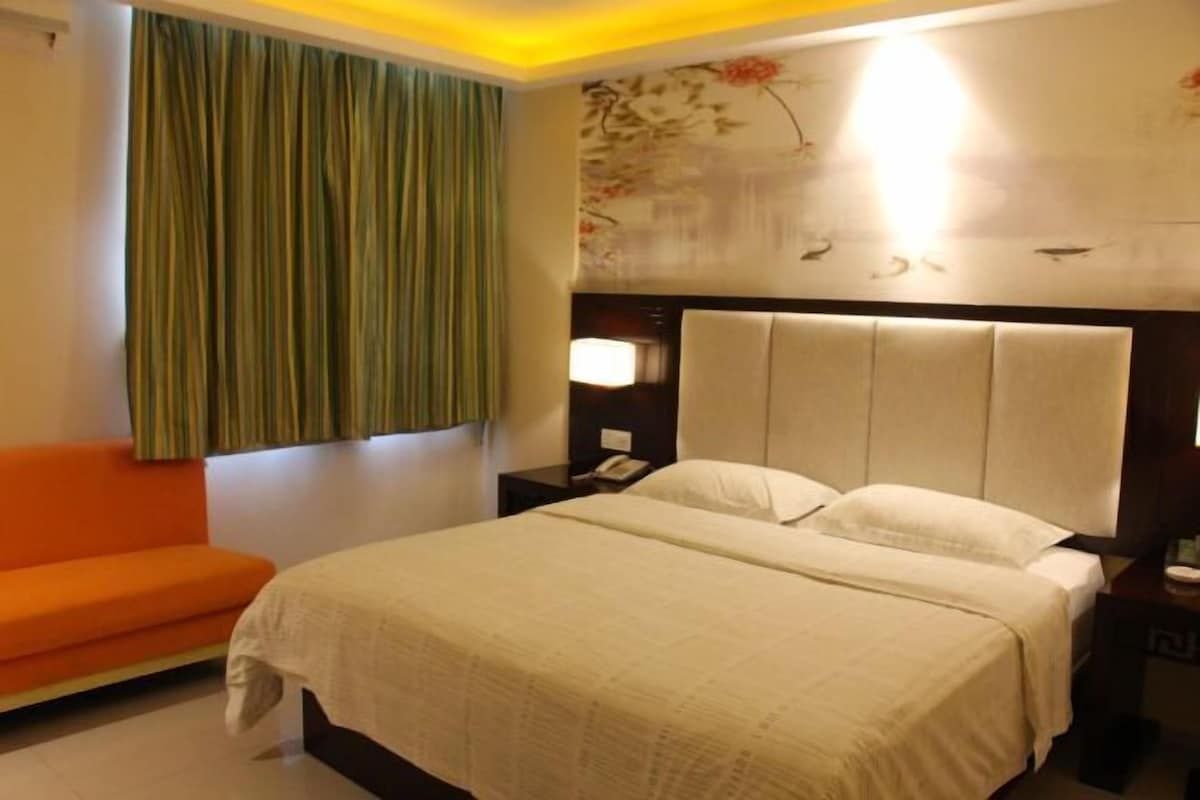 A hotel room with a bed, a nightstand, a lamp, a telephone, and a green curtain.