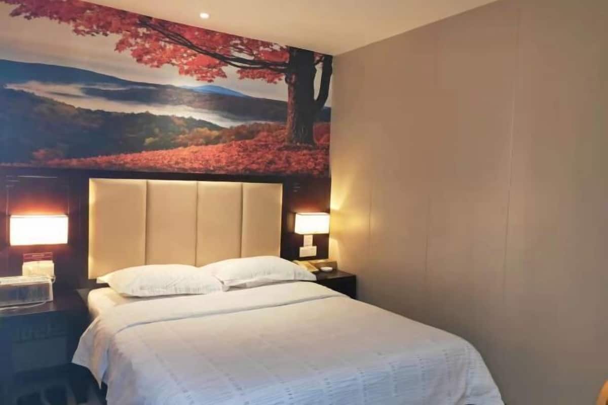 Una habitación de hotel con una cama grande, dos mesitas de noche con lámparas, y un mural de un árbol y paisaje en la pared.