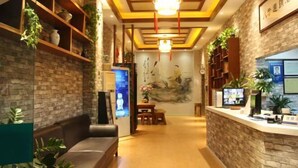 Um saguão de hotel com balcão de recepção, área de estar e plantas decorativas.