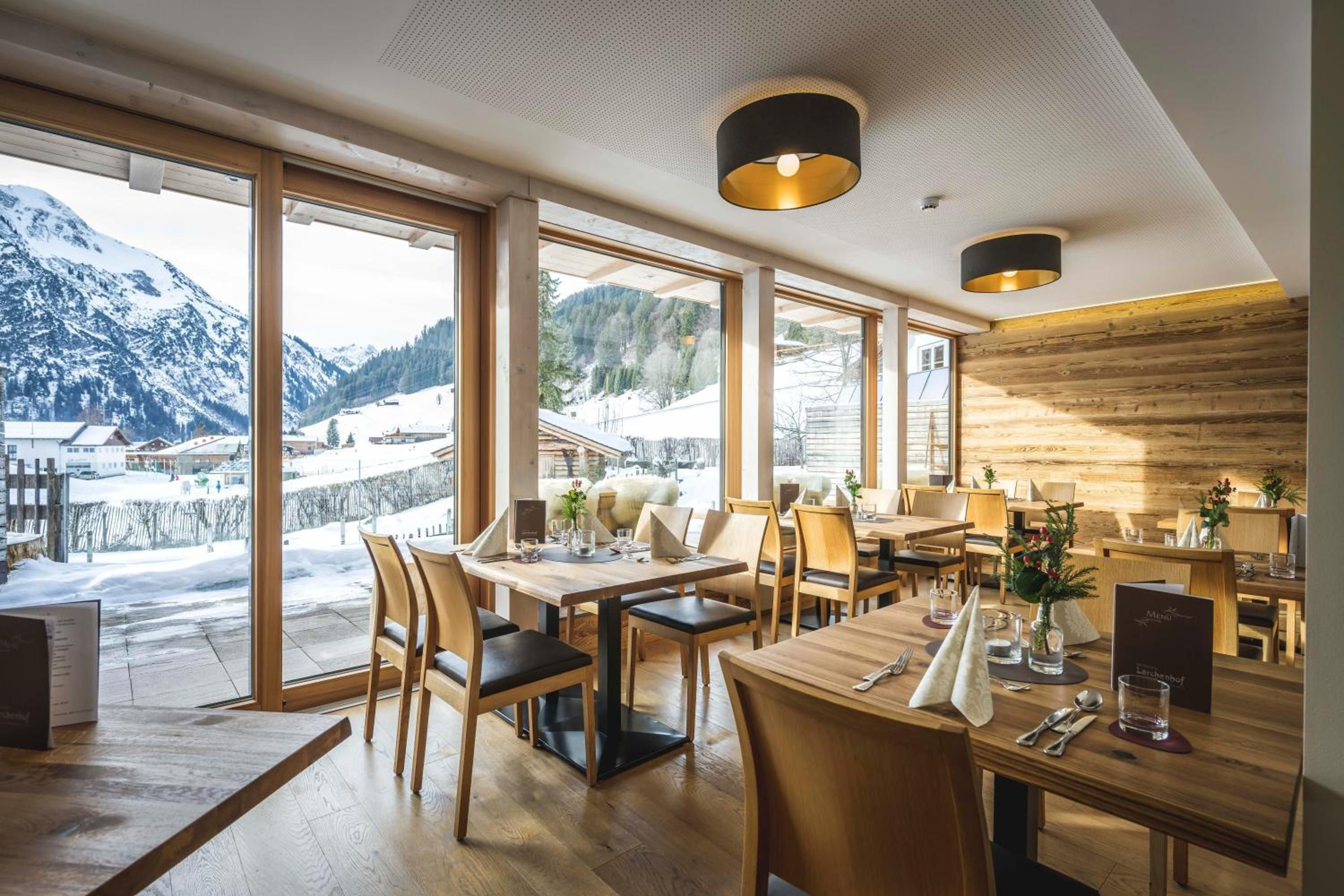 Ein Restaurant mit großen Fenstern und Blick auf die Berge, Holzmöbel und modernes Interieur.