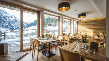 Ein Restaurant mit großen Fenstern und Blick auf die Berge, Holzmöbel und modernes Interieur.
