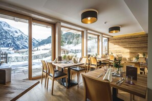A restaurant with large windows offering a mountain view, wooden furniture, and a modern interior design.