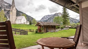 Ein Holztisch mit Stühlen auf einer Terrasse, mit Blick auf eine Kirche und Berge.
