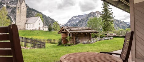 A wooden table and chairs on a patio with a view of a church and mountains.