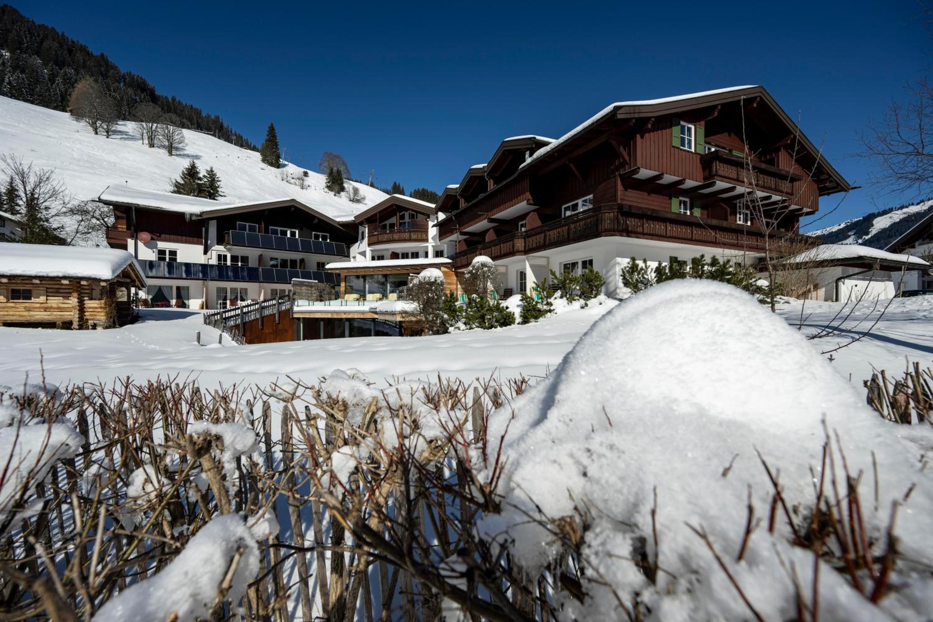 A snow-covered landscape with a large wooden chalet featuring multiple balconies and a ski lift in the background.