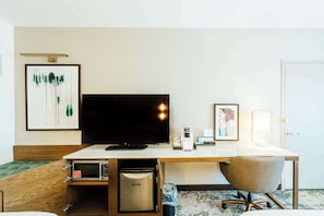 A hotel room with a bed, a desk with a computer, a television, and a microwave.
