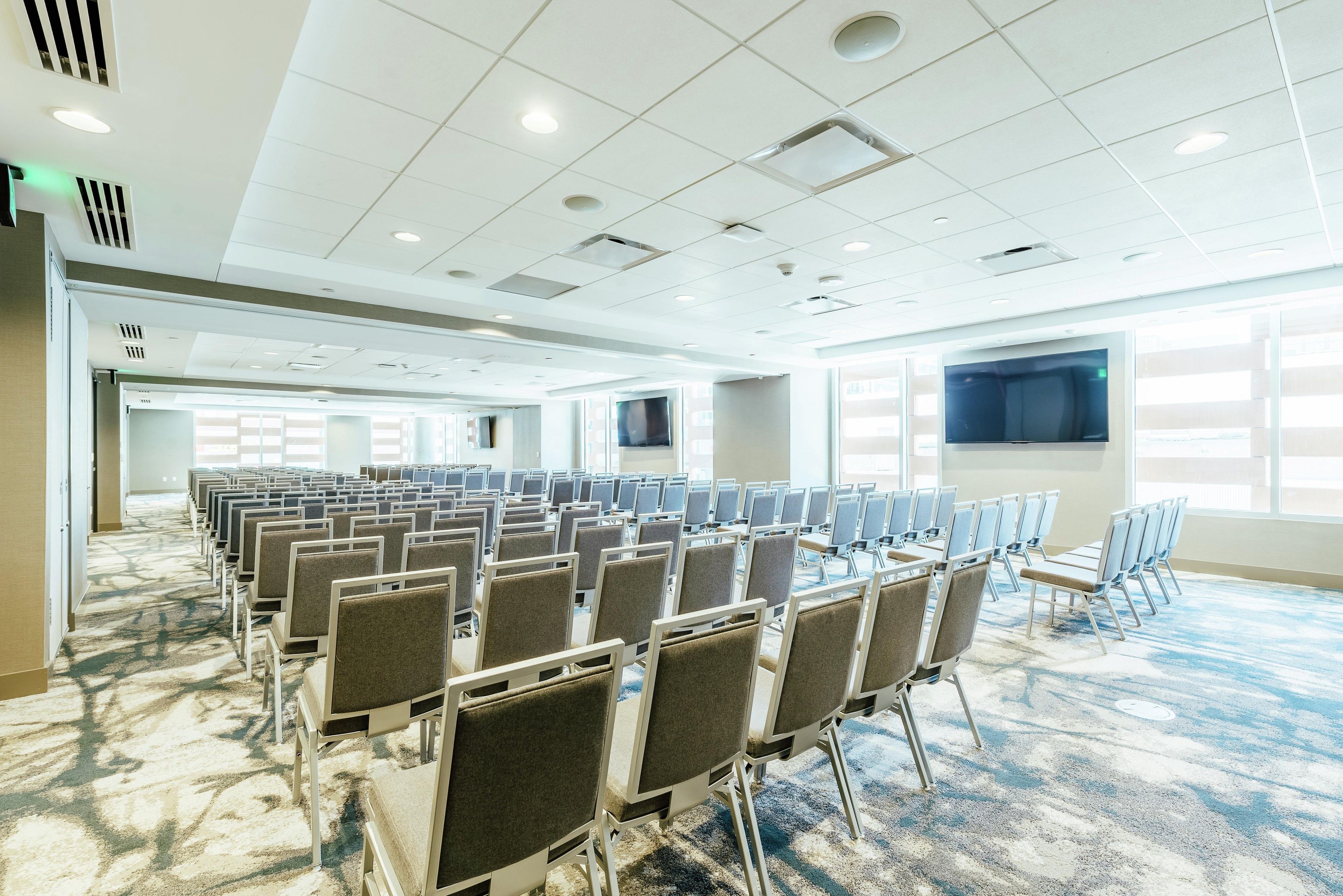 A conference room with rows of chairs, a large screen, and a carpeted floor.