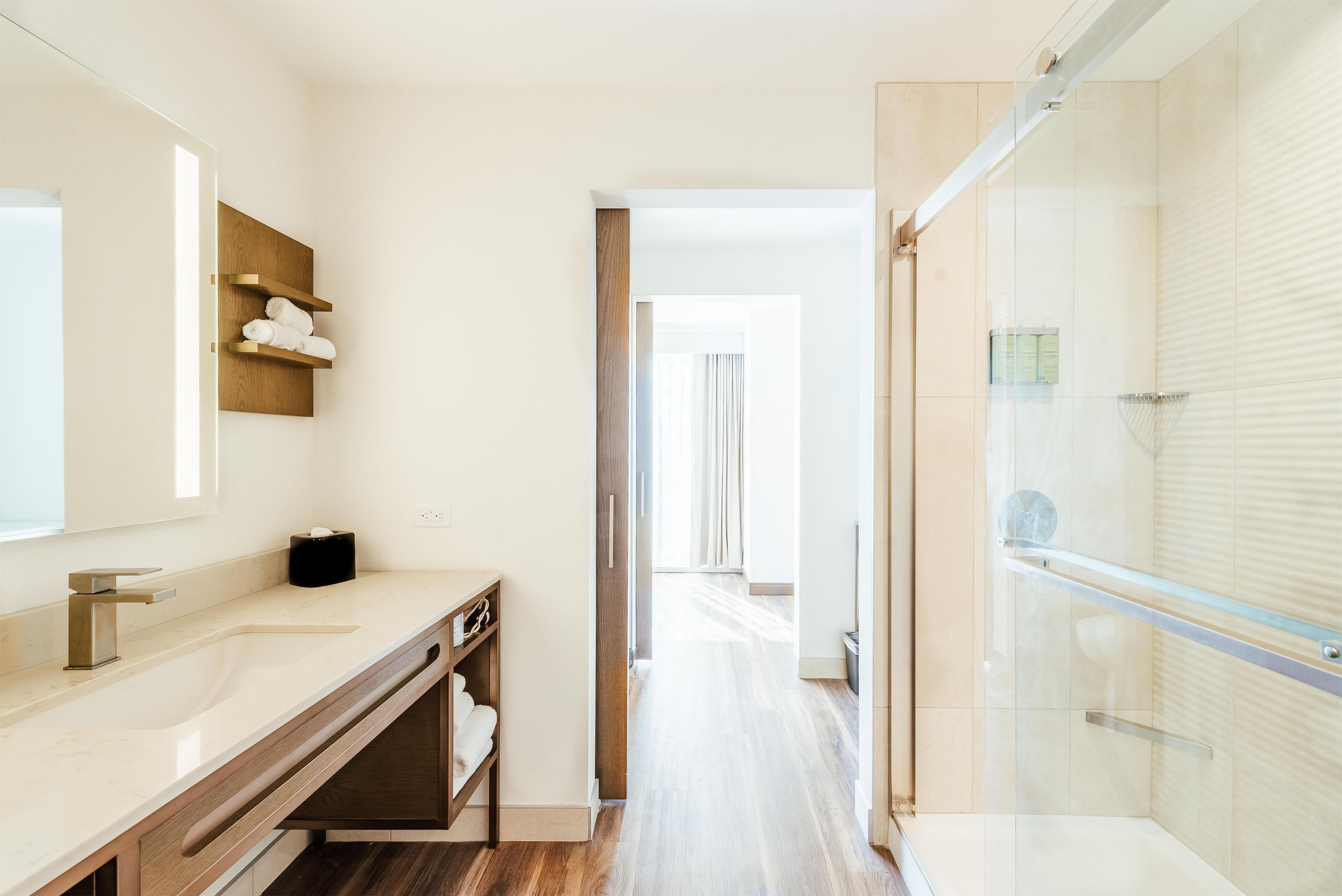 A modern bathroom with a large mirror, wooden vanity, and a glass shower enclosure.