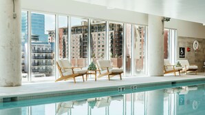 An indoor swimming pool with clear views of surrounding buildings, lounge chairs, and a visible pool lift. - Hilton Garden Inn Denver Union Station, CO (Denver)