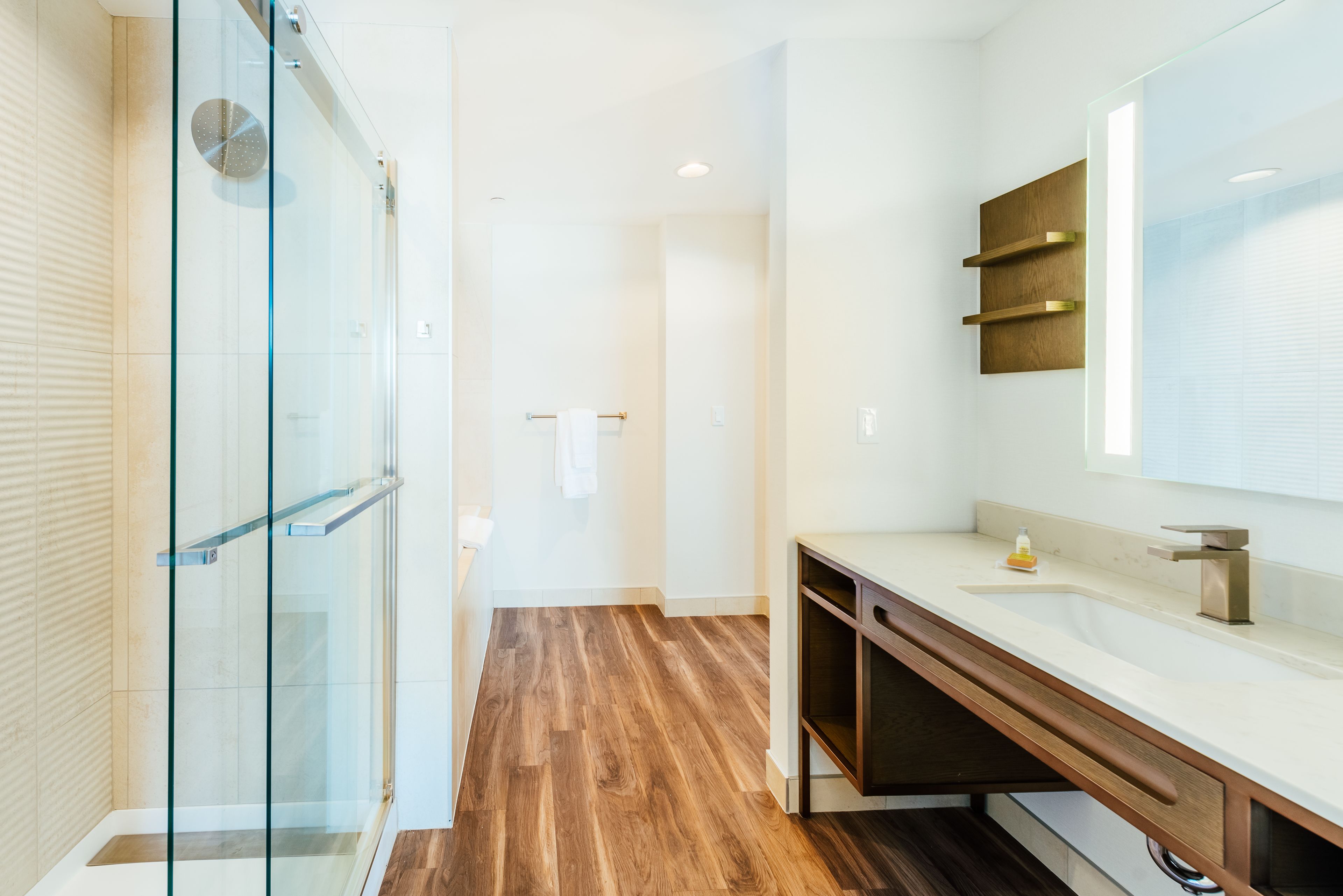 Un baño moderno con cabina de ducha de vidrio, tocador de madera y un espejo grande.