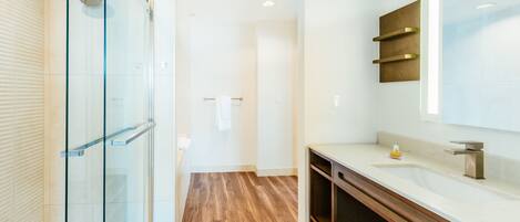 Un baño moderno con cabina de ducha de vidrio, tocador de madera y un espejo grande.
