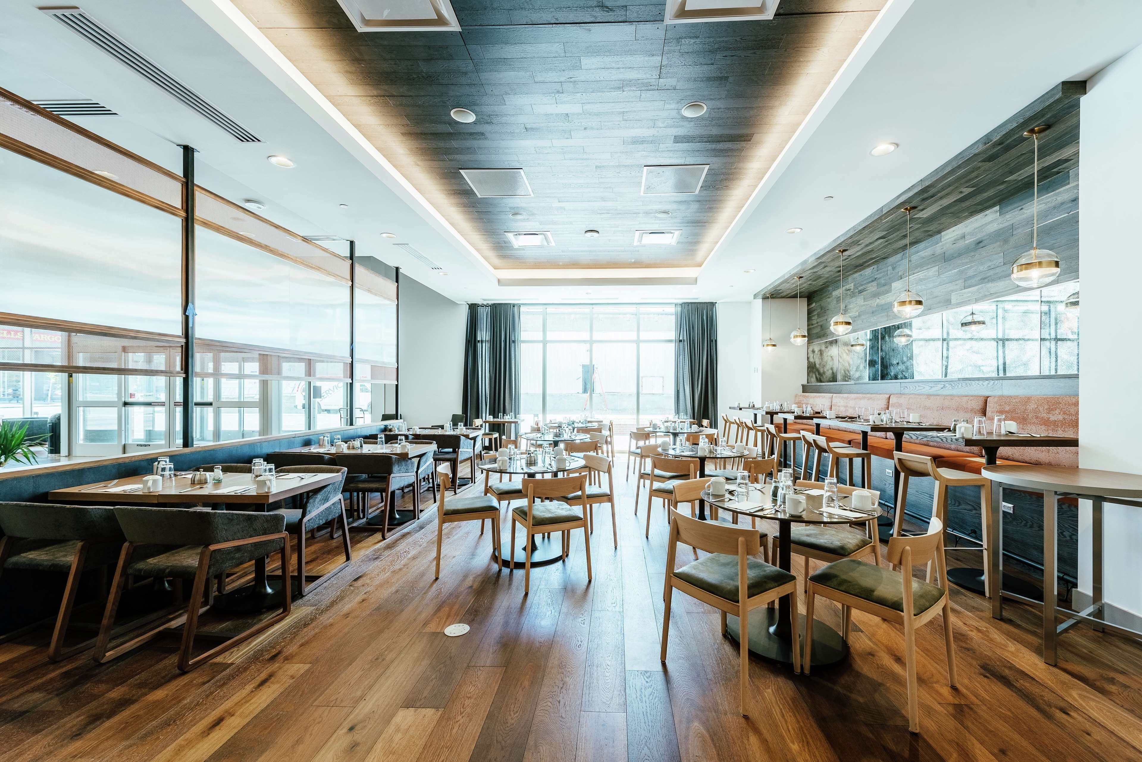 A spacious restaurant with wooden flooring, multiple seating areas, and large windows offering natural light.