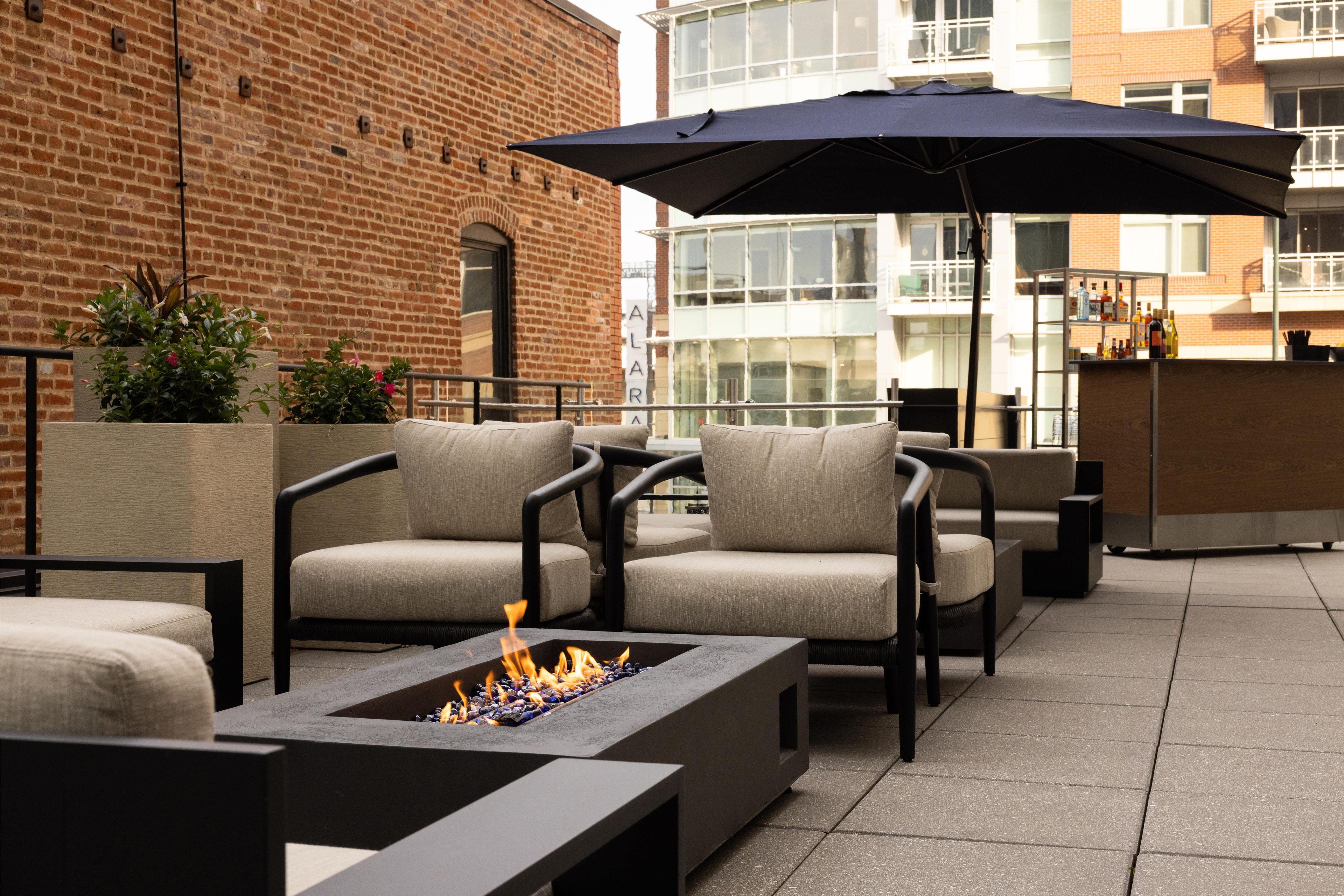 An outdoor seating area with fire pit, chairs, and a large umbrella.
