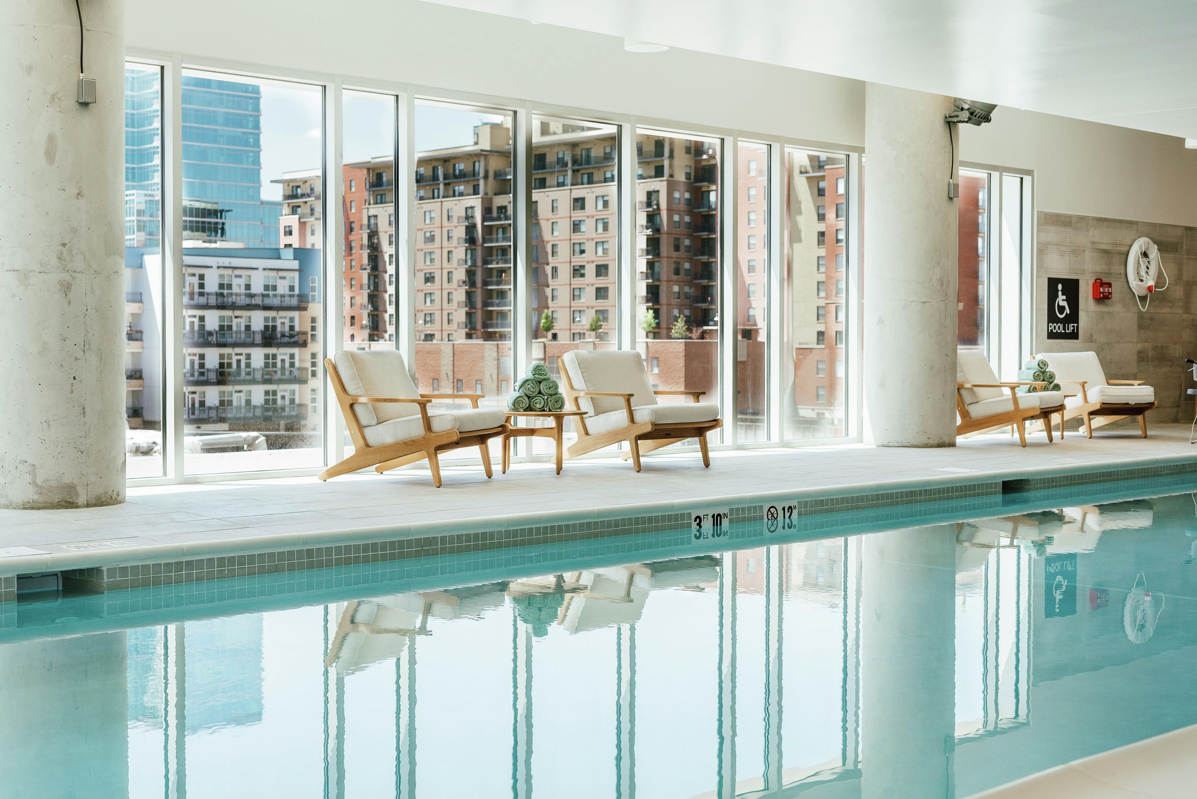 A pool area with lounge chairs and a view of the cityscape through large windows.