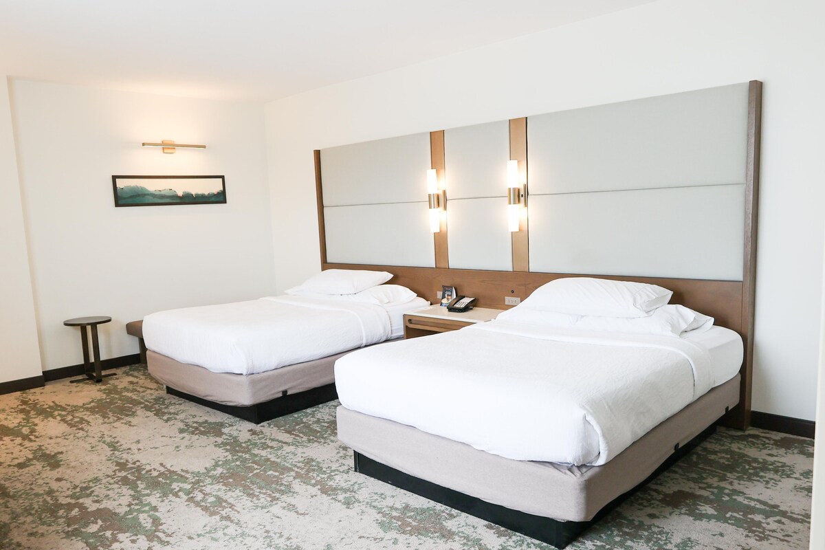 Ein Hotelzimmer mit zwei Betten, einem kleinen Tisch, einem an der Wand befestigten Telefon und einem Bild.