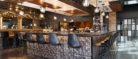 Un área de bar moderna con una isla central, taburetes y luces colgantes.