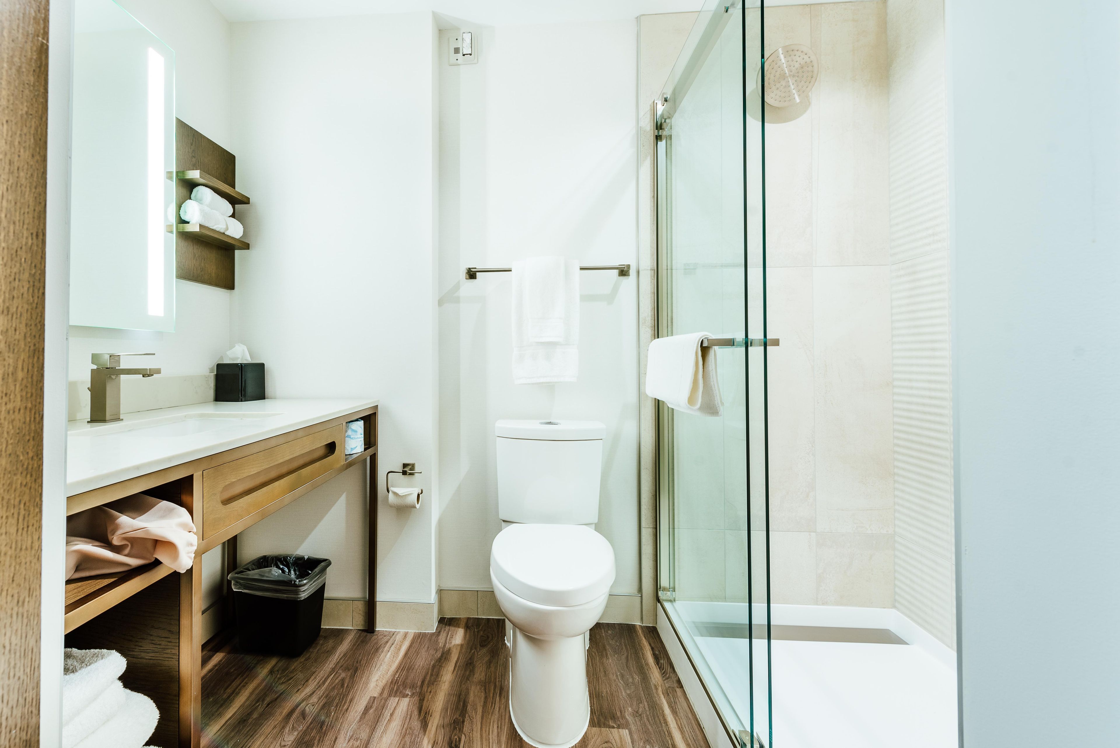 A modern bathroom with a glass shower enclosure, a wooden vanity, and a white toilet.