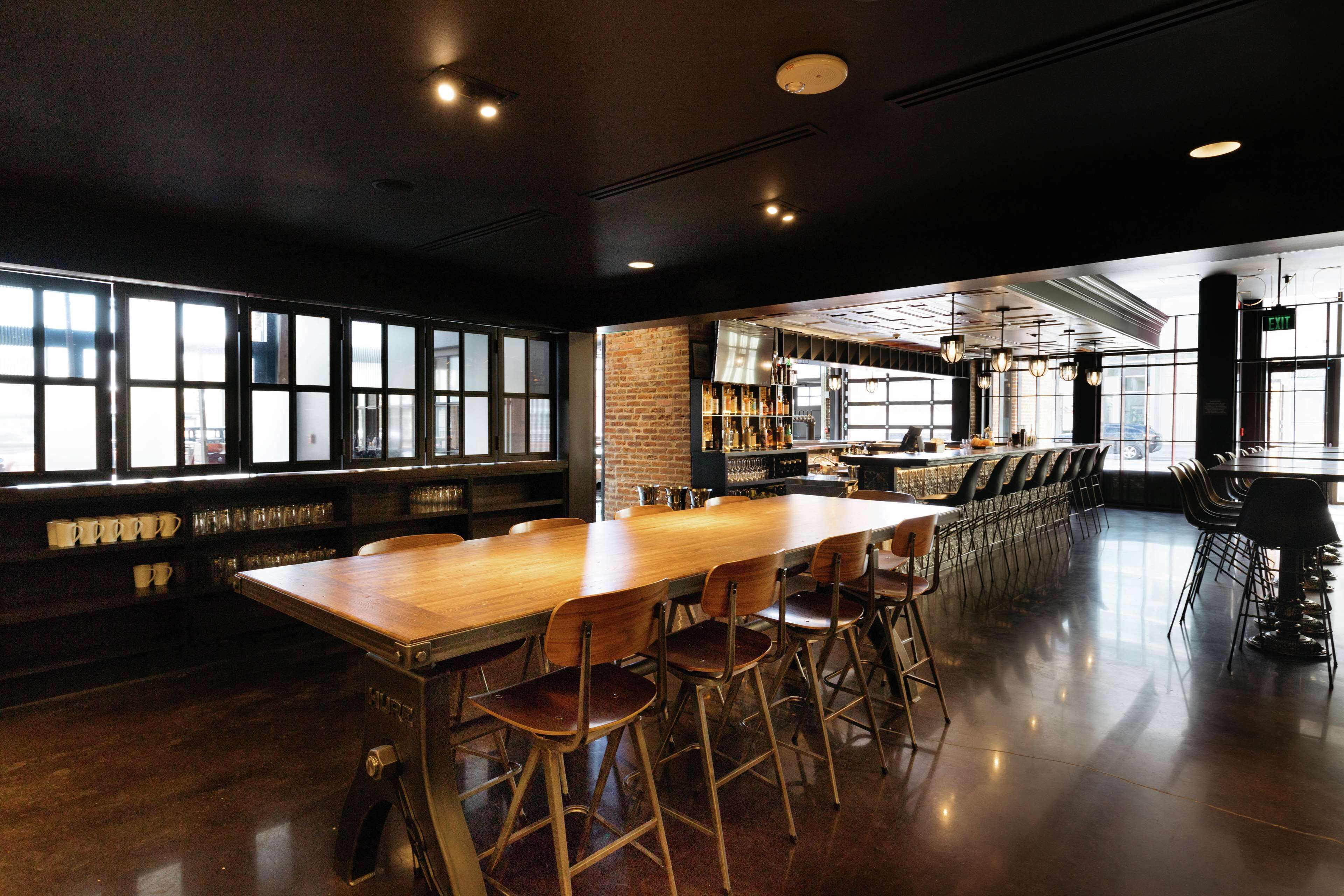 Un área de bar espaciosa con una larga mesa de madera, varios taburetes altos y una pared de ladrillo.