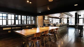 Un área de bar espaciosa con una larga mesa de madera, varios taburetes altos y una pared de ladrillo.