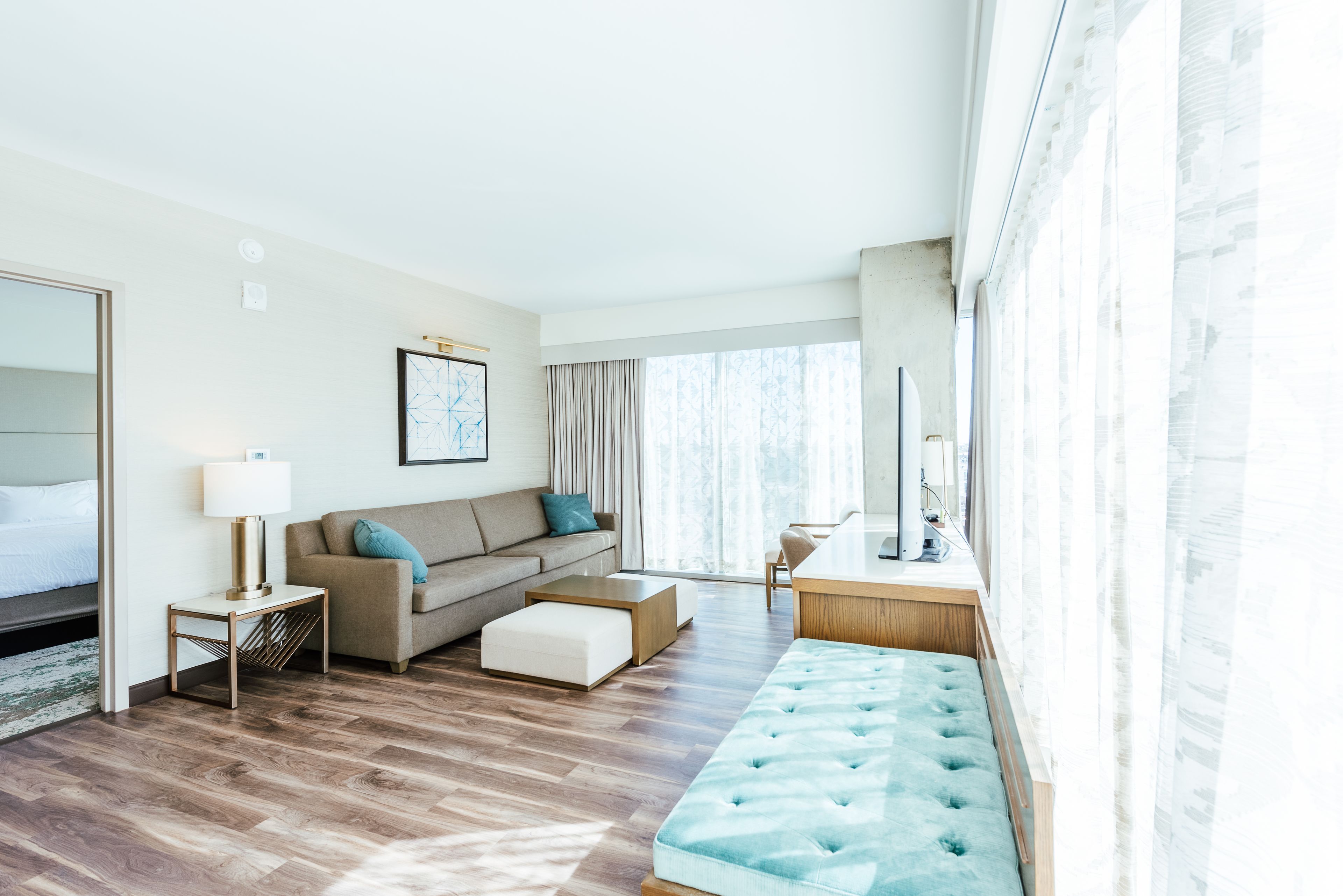 Una habitación de hotel moderna con sofá, una mesa de centro, un escritorio y un ventanal grande.
