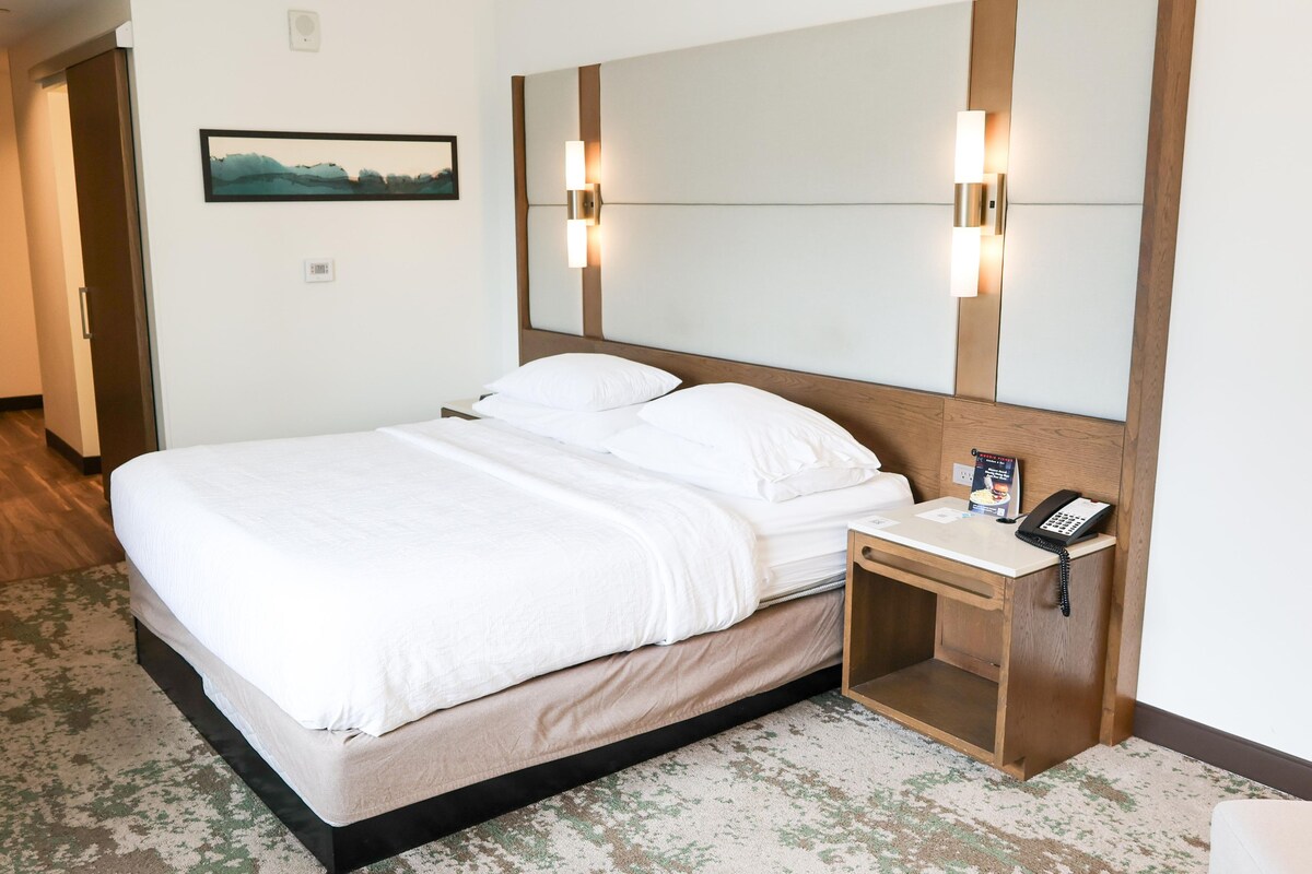 Ein Hotelzimmer mit einem großen Bett, einem Nachttisch mit Telefon und einer Wandleuchte.