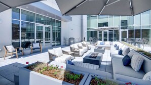 A modern outdoor seating area with white sofas, planters, and umbrellas. - Hilton Garden Inn Denver Union Station, CO (Denver)