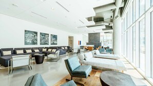 A spacious lobby with modern seating arrangements, large windows, and a high ceiling with exposed ductwork. - Hilton Garden Inn Denver Union Station, CO (Denver)
