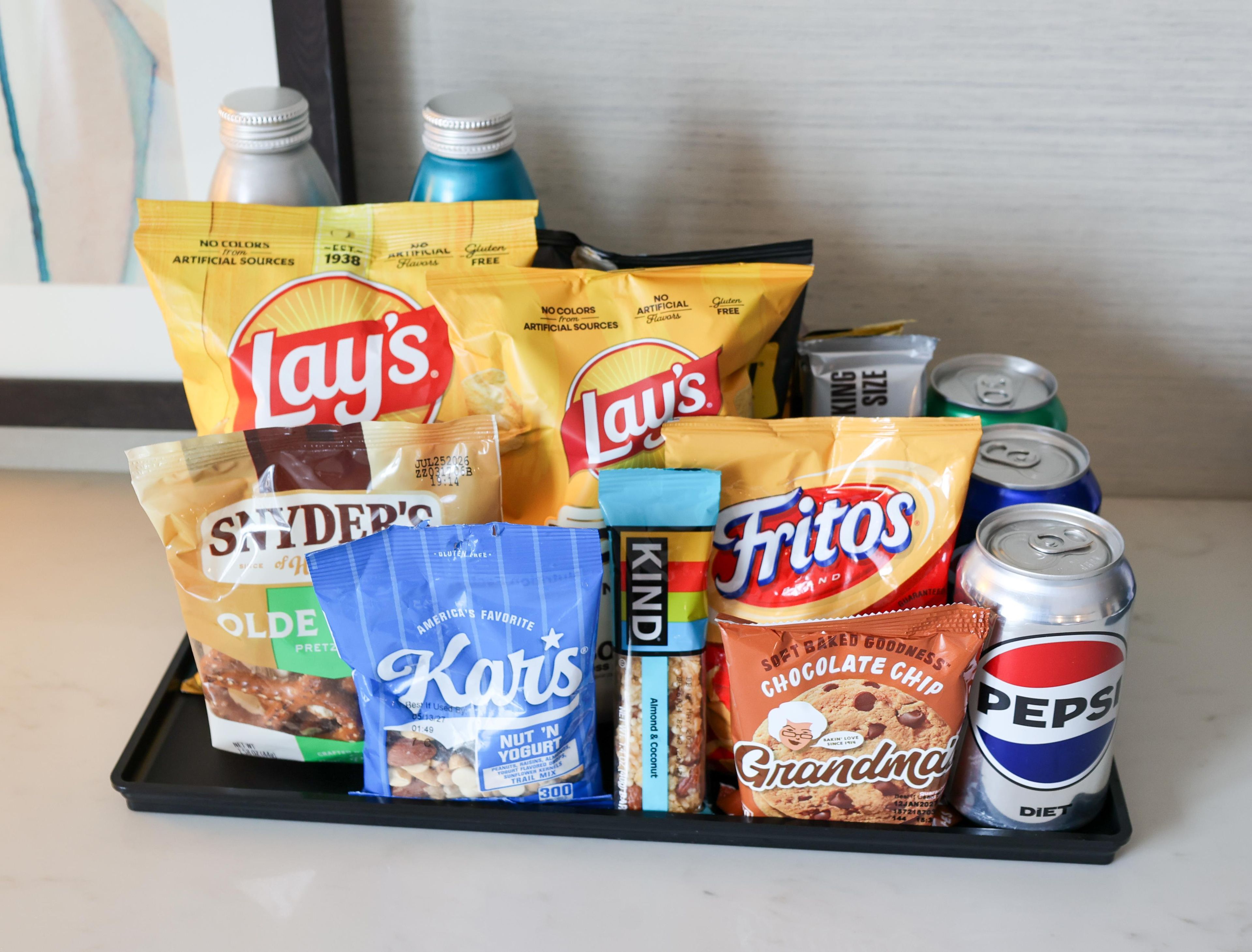 A tray with snacks and drinks including Lay's chips, Pepsi, and other packaged foods.