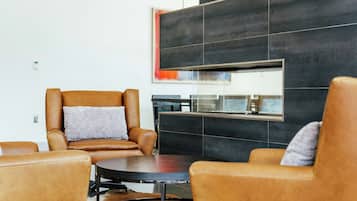 A modern living room with leather armchairs, a round coffee table, and a large black-tiled wall with a framed artwork.