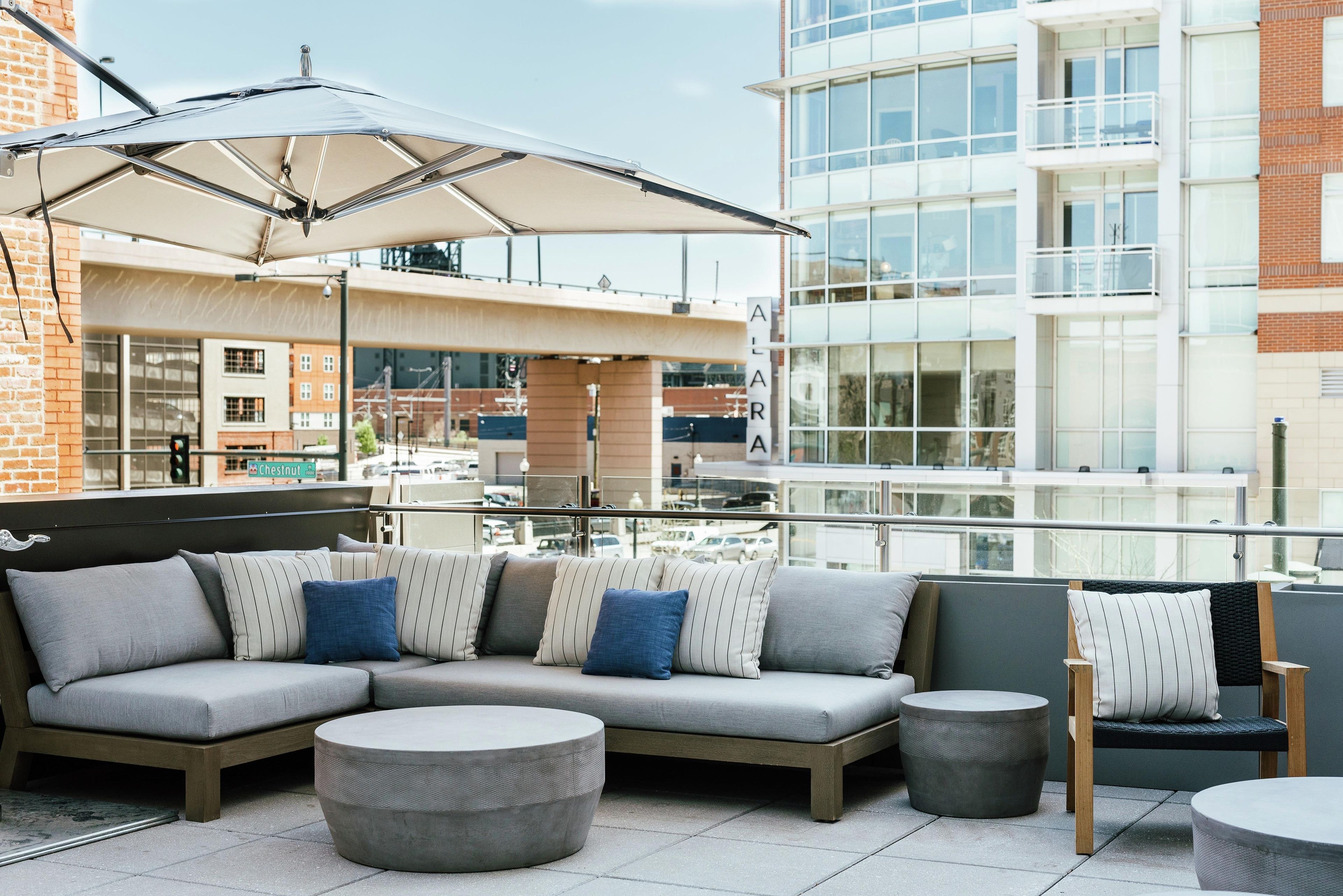 A rooftop terrace with a sectional sofa, round ottomans, and a large umbrella.