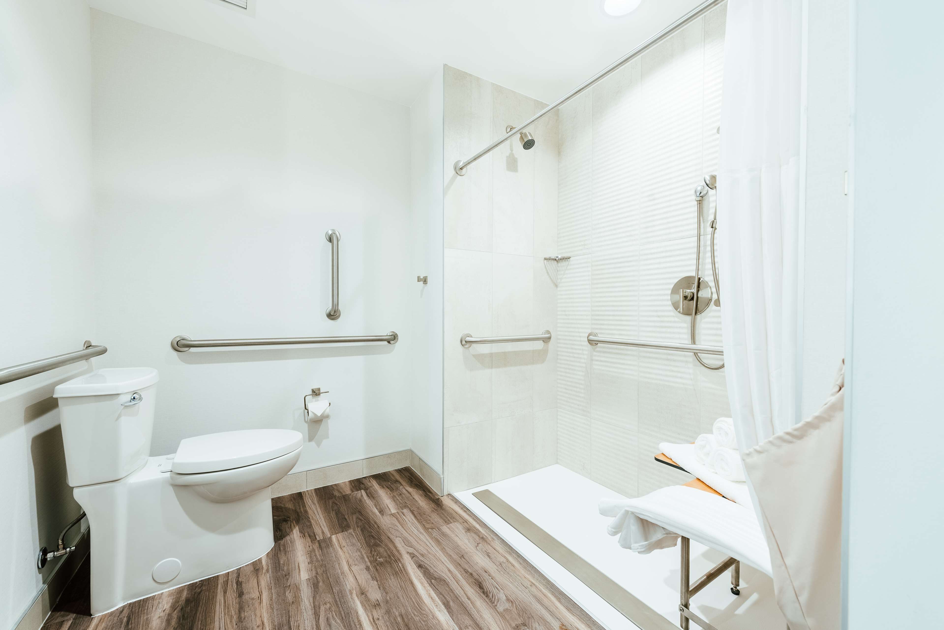 Un baño moderno con inodoro, bidé y ducha. Incluye un pasamanos y un banco con toallas.