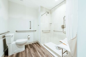 Un baño moderno con inodoro, bidé y ducha. Incluye un pasamanos y un banco con toallas.