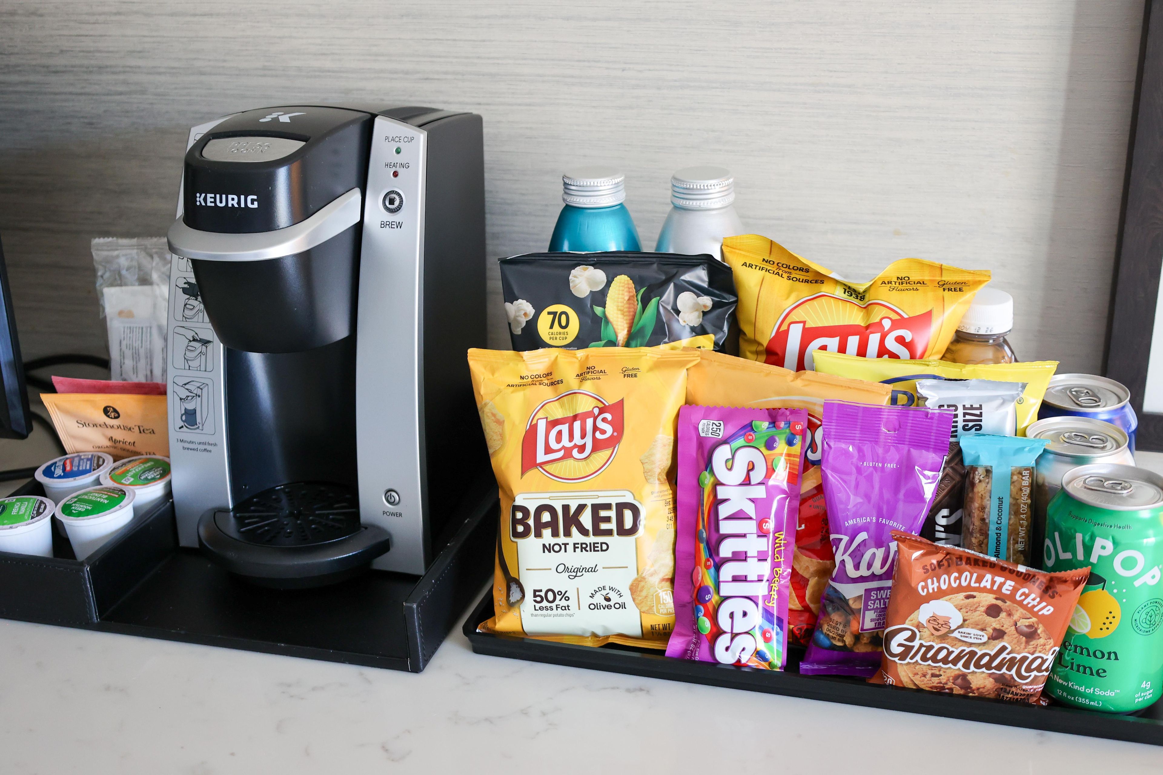 Una cafetera, varias bolsas de snacks y una lata de refresco sobre una encimera.