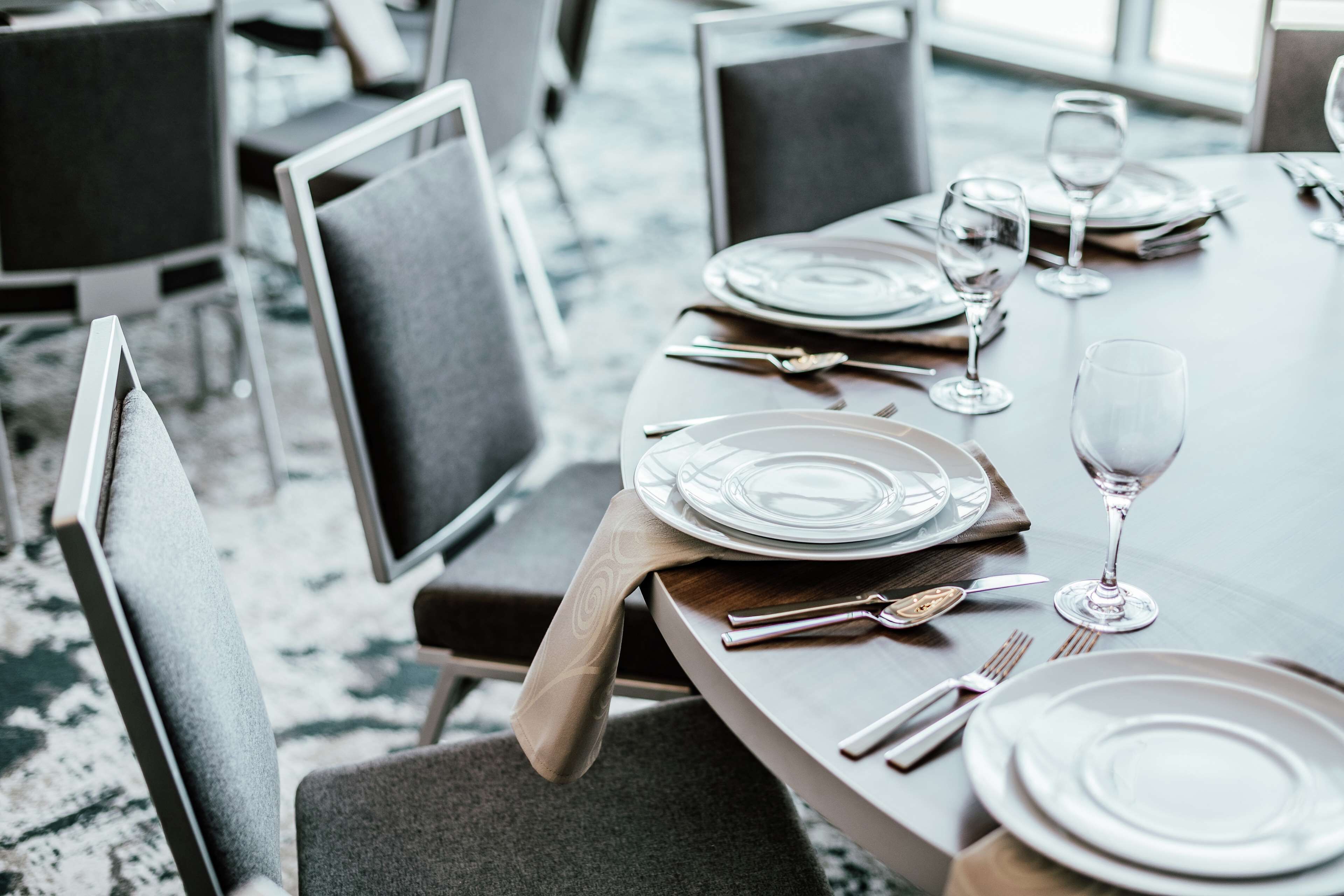 Una mesa de comedor dispuesta con platos, cubiertos y copas de vino, rodeada de sillas modernas.