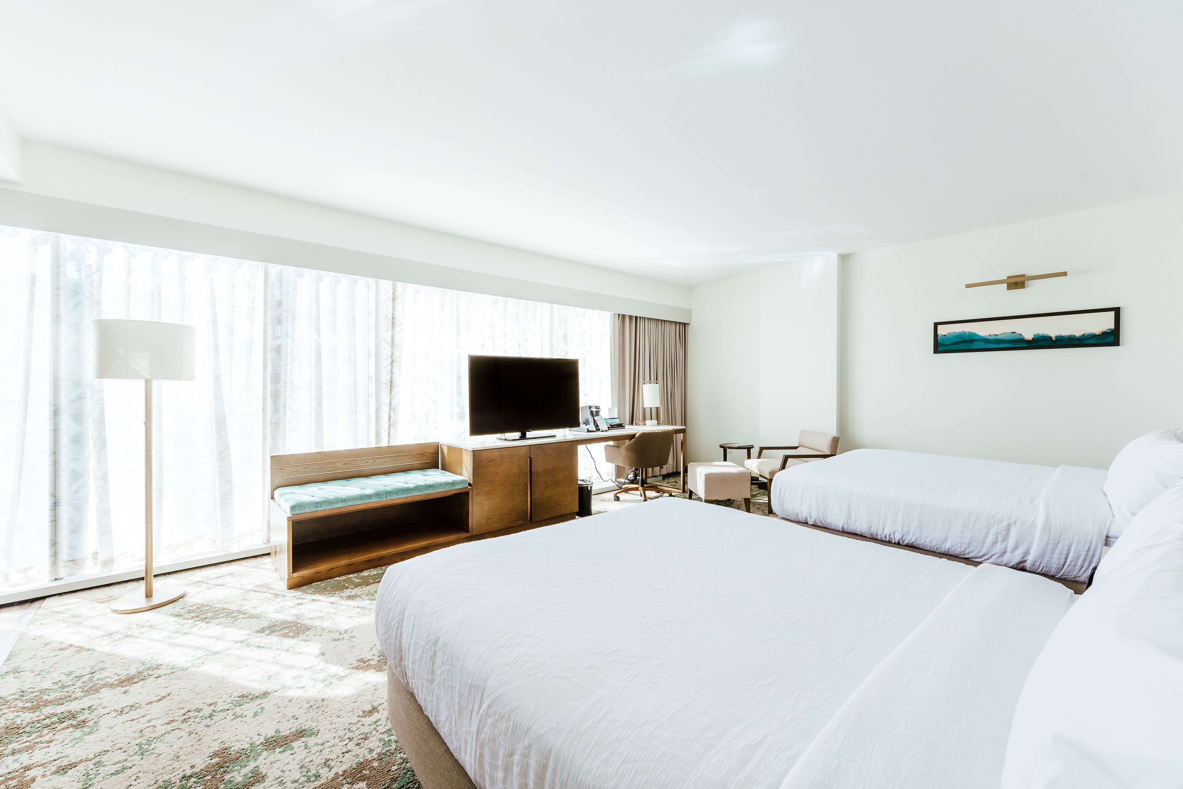 Camera d'albergo con un letto grande, una scrivania con televisore, una sedia e una finestra con tende.