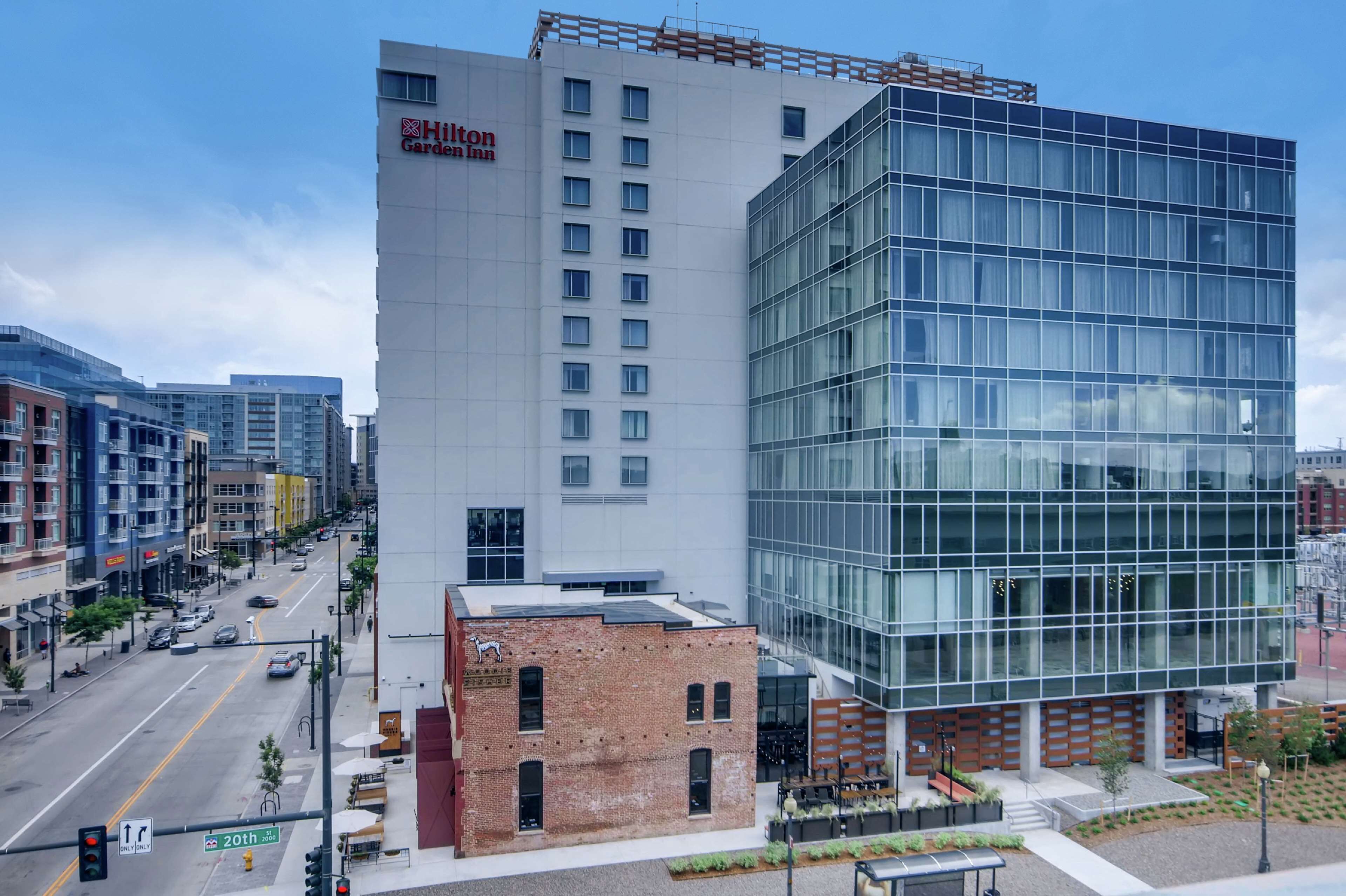 Un hôtel Hilton Garden Inn doté d’une façade moderne en verre, situé à un carrefour de la ville, à un endroit où les rues et les feux de signalisation sont bien visibles.