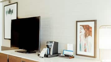 A hotel reception desk with a flat-screen TV, a coffee machine, a framed artwork, and a lamp.