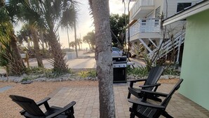 An outdoor patio area with two black Adirondack chairs, a barbecue grill, and a tree. - Charming Old Florida Beach Cottage with Gulf View - Just 60 Steps to Beach! (Manasota Key)