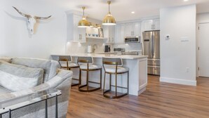 Una cocina moderna con armarios blancos, electrodomésticos de acero inoxidable y una isla central con taburetes de bar.